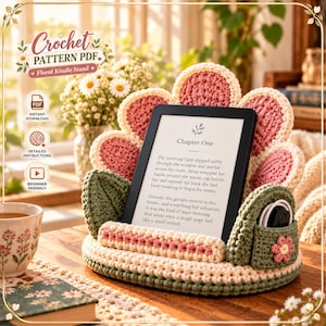 May include: A crochet Kindle stand shaped like a flower with pink petals, a cream base, and green leaves. The stand holds an e-reader displaying text that begins with Chapter One. A small green pocket on the side holds a charging cable.
