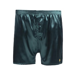 Op de afbeelding: Donker smaragdgroene boxershorts met een gladde, satijnachtige afwerking. Deze short heeft een elastische tailleband, een centrale knoopsluiting aan de voorzijde en een klein rechthoekig label met gouden tekst op de rechter broekspijp.