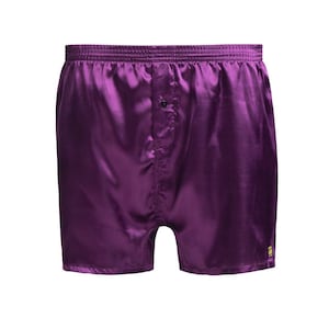 Puede incluir: Unos calzoncillos tipo bóxer de satén en color morado intenso con cintura elástica, bragueta central con un solo botón negro y una pequeña etiqueta rectangular amarilla de la marca cosida en el dobladillo de la pierna derecha.