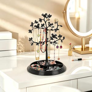 May include: A black jewelry stand shaped like a tree with branches for hanging necklaces and earrings. The base is a circular tray with three compartments for storing rings and small accessories. The tree features bird and leaf silhouettes.