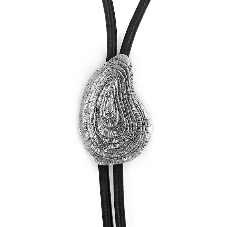 May include: A silver bolo tie with a textured, circular design. The tie is made of leather and has a silver clasp.