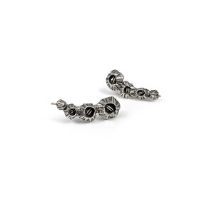May include: A pair of silver earrings with a unique, organic design. Each earring features a series of small, rounded shapes that resemble flowers or shells.