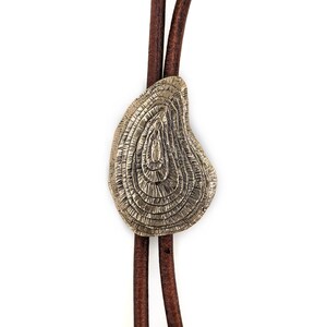 May include: A brown leather bolo tie with a silver, circular, textured pendant. The pendant has a concentric circle design.