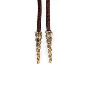 May include: A pair of brown leather cords with gold-colored spiral-shaped tips.