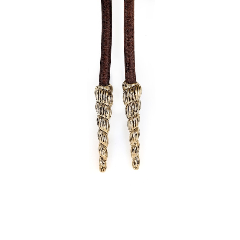 May include: A pair of brown leather cords with gold-colored spiral-shaped tips.