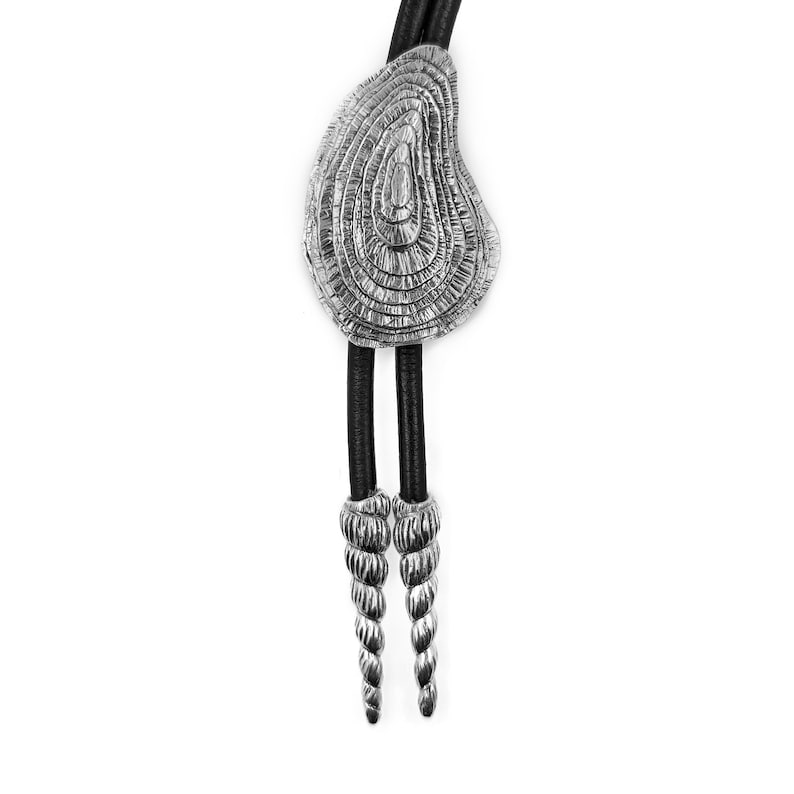 May include: A silver bolo tie with a textured, circular pendant and two spiral-shaped ends. The tie is made of black leather.