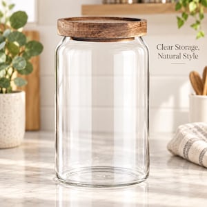 Peut inclure: Un bocal de rangement en verre transparent avec un corps cylindrique et un couvercle rond en bois brun foncé. Le texte Clear Storage, Natural Style est imprimé sur le côté droit. Le bocal présente une surface lisse et une base plate.