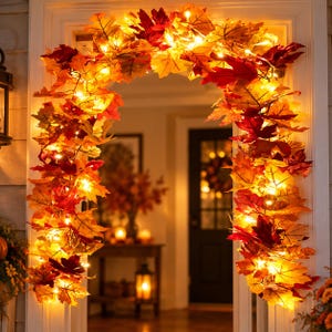 Könnte beinhalten: Eine künstliche Herbstblattgirlande, die über einem Türrahmen drapiert ist und aus einer Mischung aus roten, orangen und gelben Ahornblättern besteht, durchsetzt mit warmweißen Lichterketten, die das Laub durchgehend beleuchten.