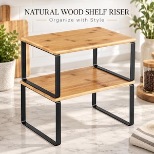 May include: A two-tier shelf riser featuring natural wood surfaces and black metal frames. The text NATURAL WOOD SHELF RISER Organize with Style is visible above the unit. The structure consists of two rectangular wooden platforms supported by black metal legs.