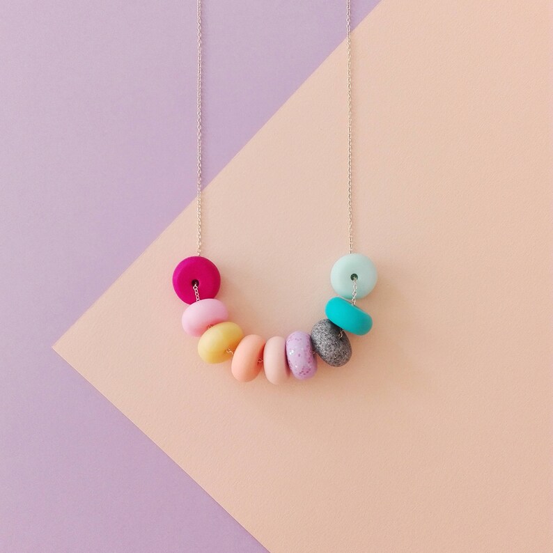 May include: A colourful necklace with round, pastel-coloured beads. The beads are arranged in a rainbow pattern, starting with pink and ending with turquoise.