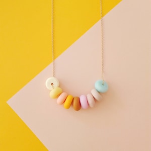 May include: A pastel-coloured necklace with a gold chain and round beads. The beads are in shades of yellow, orange, pink, and blue.