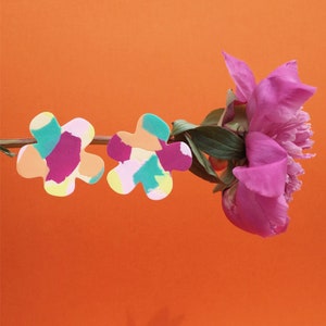 Op de afbeelding: Een paar kleurrijke, bloemvormige oorbellen met een abstract patroon in roze, oranje, geel en groen. De oorbellen zijn gemaakt van polymer clay en zijn handgemaakt.
