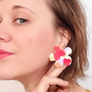 May include: A pair of colorful abstract flower-shaped earrings. The earrings are made of polymer clay and have a white, pink, orange, and purple color scheme.