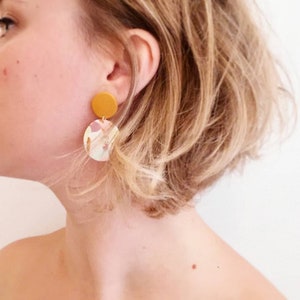 May include: A pair of dangle earrings with a round, yellow top and a round, white bottom with pink and gold abstract patterns.