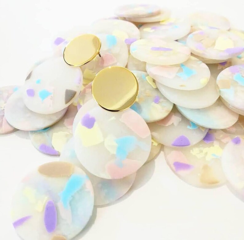 May include: A pair of gold tone earrings with white, pink, blue, and yellow confetti-like designs. The earrings are made of multiple layers of round, flat, acrylic pieces.