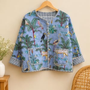May include: A light blue quilted jacket featuring a tropical print with palm trees, parrots, toucans, and leopards. The jacket has a round neckline, long sleeves with striped cuffs, a front button closure, and two square front pockets with striped trim.