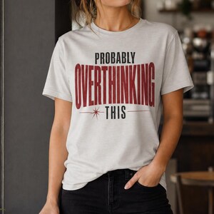May include: A light grey short-sleeved t-shirt featuring the black text "PROBABLY" above the large, bold, dark red text "OVERTHINKING" and the black text "THIS" underlined with a thin line and a small starburst graphic.