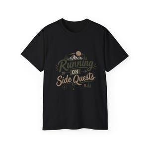 May include: A black short-sleeved t-shirt featuring a graphic design with the text Running ON Side Quests. The illustration includes a mountain range, a sun, pine trees, an arrow, a compass, and a dotted path with a location pin icon.