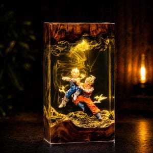 May include: A rectangular resin lamp featuring a dark wood base and top, enclosing two fighting anime figures in dynamic poses. The interior is filled with swirling golden light effects and jagged lightning bolts, creating a glowing, energetic scene.