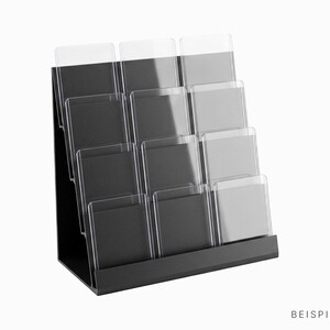 Könnte beinhalten: Ein schwarzer, gestufter Präsentationsständer mit zwölf transparenten Acrylfächern, die in vier Reihen zu je drei angeordnet sind. Die Struktur ist zur besseren Sichtbarkeit geneigt und enthält den Text BEISPIELBILD unten rechts.