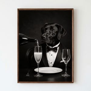 May include: A black and white framed wall art print featuring a black Labrador dog wearing a black tuxedo jacket with a white shirt and black bow tie. A bottle pours sparkling liquid into a glass next to an empty plate and a second glass.