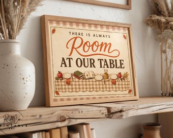 May include: A rectangular framed wall art print featuring a beige background with a brown checkered border. The text reads THERE IS ALWAYS Room AT OUR TABLE. Below the text is an illustration of a table set with plates, books, and apples.