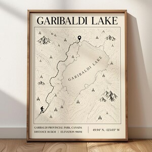 May include: A framed wall art print featuring a topographic map of Garibaldi Lake in Garibaldi Provincial Park, Canada. The beige map displays a dotted hiking trail, mountain icons, a location pin, and text including coordinates and 18.5km distance.