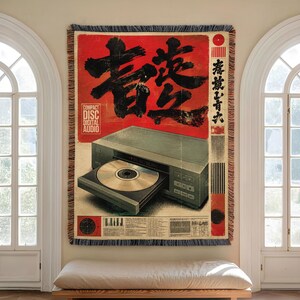 May include: A rectangular woven throw blanket featuring a graphic design of a grey CD player with an open disc tray. The background is a vibrant red with large black Japanese calligraphy, the text Compact Disc Digital Audio, and technical details.