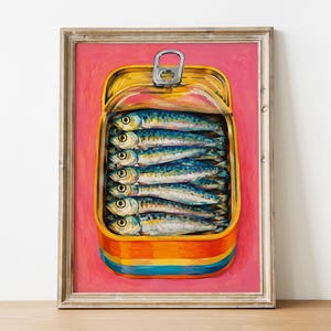 May include: A framed painting of an open yellow tin can filled with six stacked sardines. The tin features a silver pull tab at the top and horizontal blue and orange stripes at the base. The background is a solid, vibrant pink colour.