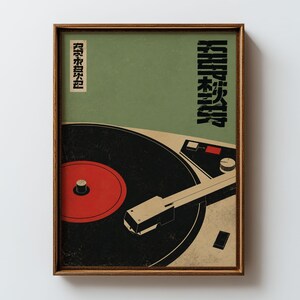 May include: A framed wall art print featuring a stylized illustration of a record player with a black vinyl disc and a red center label. The background is a muted olive green with black Japanese text characters arranged vertically on the right side.
