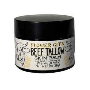 May include: A black jar of Flower City Beef Tallow Skin Balm with a white label featuring black cow illustrations and yellow floral accents. The text reads: Flower City Beef Tallow Skin Balm, small batch, locally sourced, 100% grass-fed tallow, Net Wt. 1.0 oz (28g).