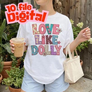 May include: A white short-sleeve t-shirt featuring the text LOVE LIKE DOLLY in large, multi-colored, patterned block letters with floral, plaid, and polka dot designs. The shirt is paired with light blue striped shorts and a small canvas tote bag.