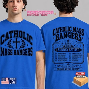 May include: A bright blue t-shirt featuring black screen-printed graphics. The front displays the text CATHOLIC MASS BANGERS with a cross and laurel leaves. The back lists a Sunday Setlist of ten hymns under the same title.
