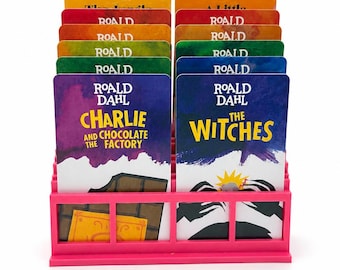 May include: A bright pink plastic display stand holding two rows of Roald Dahl book covers. The front cards feature the titles Charlie and the Chocolate Factory and The Witches, with colorful illustrations and text printed on each card.