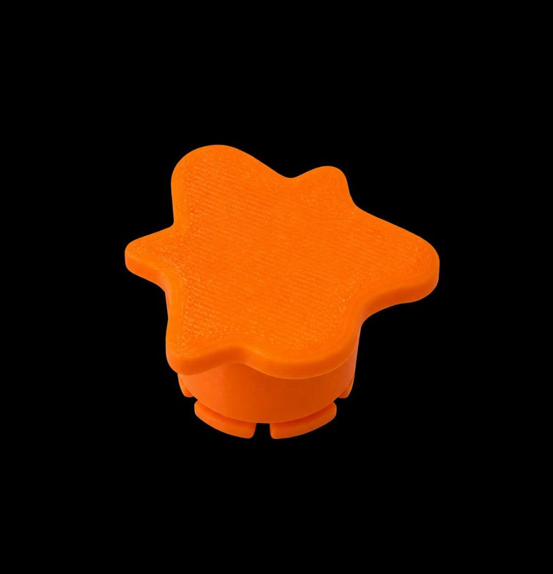 May include: A bright orange knob with a five-pointed star-like shape. The top surface features a textured finish, while the base is cylindrical with small, evenly spaced vertical notches around the bottom edge, set against a black background.