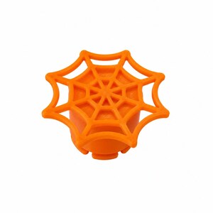 May include: A bright orange knob featuring a raised spider web design on its circular top surface. The object has a solid cylindrical base with a textured exterior and a flat, webbed pattern extending outward from the center to the edges.