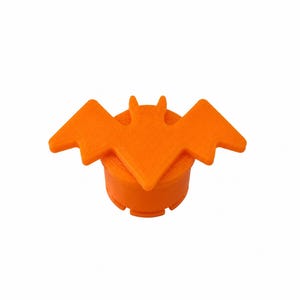 May include: A bright orange bottle stopper featuring a flat, stylized bat silhouette attached to the top. The cylindrical base has a textured surface with visible horizontal lines, and the bat has pointed ears and outstretched wings.