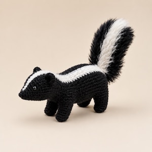 May include: A crocheted skunk figurine featuring a black body with a white stripe running from the nose to the back. The skunk has a large, fluffy, upright tail with black and white fur-like texture and small black eyes on its head.