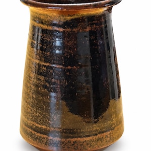 May include: A cylindrical ceramic vase with a flared rim, featuring a glossy glaze in shades of deep black and earthy brown. The surface displays a mottled, textured appearance with horizontal bands of colour transitioning from dark to light tones.