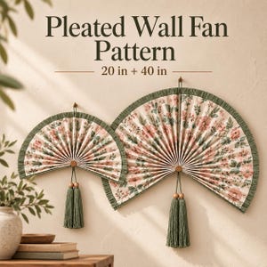May include: Two semi-circular pleated wall fans with a floral pattern of pink flowers and green leaves on a cream background. Each fan features a dark green fringed border, a central wooden bead, and a long green tassel. Text reads: Pleated Wall Fan Pattern 20 in + 40 in.