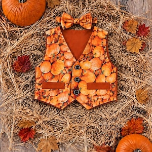 Puede incluir: Un chaleco sin mangas y una pajarita a juego con un estampado integral de calabazas naranjas. El chaleco tiene un cuello en V, tres botones oscuros en el centro y dos bolsillos rectangulares. La tela muestra un patrón repetido de calabazas.