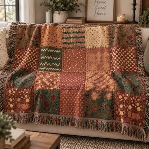 Könnte beinhalten: Eine gewebte Wohndecke mit einem Patchwork-Design aus verschiedenen Quadraten in Rost-, Waldgrün- und Cremetönen. Das Muster umfasst florale Motive, Punkte und Zickzacklinien, abgerundet durch dekorative Fransen an den Rändern.