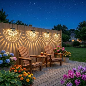 Könnte beinhalten: Vier schwarze, halbkreisförmige Solar-Wandleuchten an einem Holzzaun, die komplizierte fächerförmige Lichtmuster werfen. Zwei Holzstühle stehen auf einer Terrasse mit blauen, rosa und orangefarbenen Blumen unter einem klaren Nachthimmel.