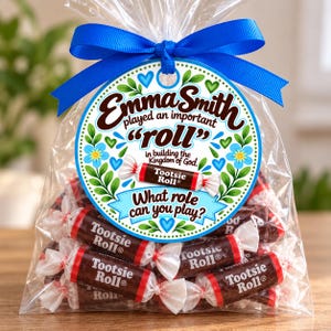 May include: A clear plastic bag filled with brown Tootsie Roll candies, tied with a blue ribbon. A round tag features the text Emma Smith played an important roll in building the Kingdom of God. What role can you play? with floral accents.