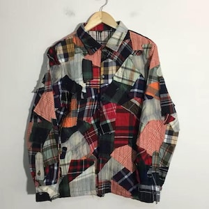 Peut inclure: Une chemise à manches longues boutonnée présentant un motif en patchwork composé de divers tissus à carreaux et écossais dans des tons de rouge, bleu marine, orange, vert, jaune, blanc et gris, avec un col et des poignets classiques.