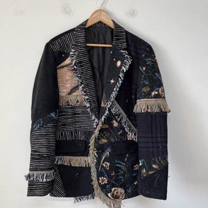 May include: A patchwork blazer featuring a mix of black, white, and multi-coloured fabrics. The garment includes panels of striped, floral, and plaid patterns with frayed edges along the lapels, pockets, and cuffs. It has a single-button closure.