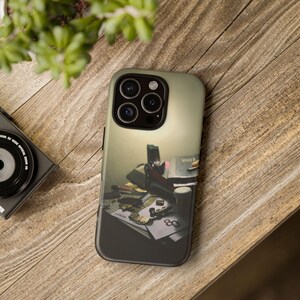 May include: A smartphone case featuring a photographic print of a cluttered desk surface with various objects including a gold chain, a small pipe, and papers with the text Lamar and 80 visible, all set against a soft, neutral-toned background.