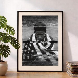 Pode incluir: Um poster emoldurado a preto e branco com um retrato de A$AP Rocky envolto numa bandeira americana. A imagem tem um efeito de glitch horizontal e uma barra retangular preta no centro com o texto branco A$AP ROCKY LONG.LIVE.A$AP.