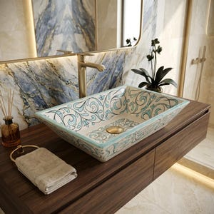 May include: A rectangular ceramic vessel sink featuring a white base with intricate light blue and dark blue swirling floral patterns. The sink includes a gold-toned drain plug and is paired with a tall, brushed gold faucet on a dark wood vanity.