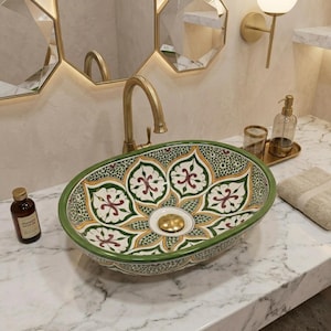 May include: An oval ceramic vessel sink featuring a hand-painted floral pattern in shades of green, yellow, and maroon on a white background. The sink has a gold-toned drain and is paired with a matching gold-toned faucet on a marble countertop.